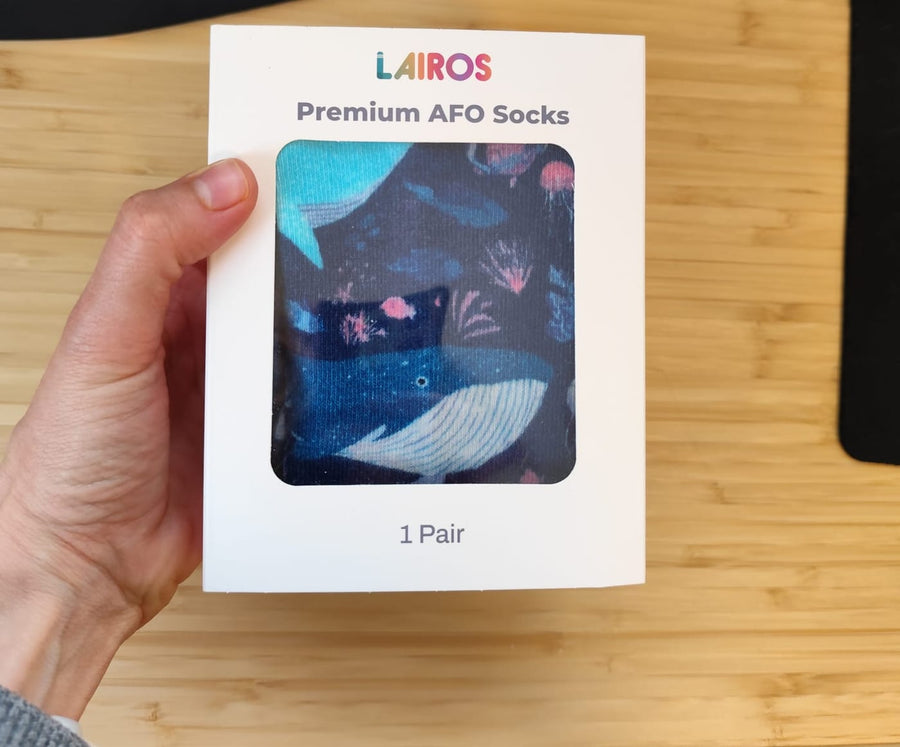A hand holding a Lairos gift box with a window showing the printed socks inside